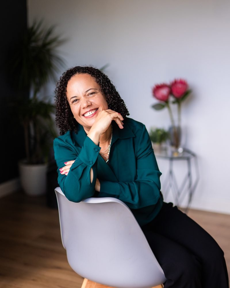 Alicia Noble laughing, seated on a grey chair