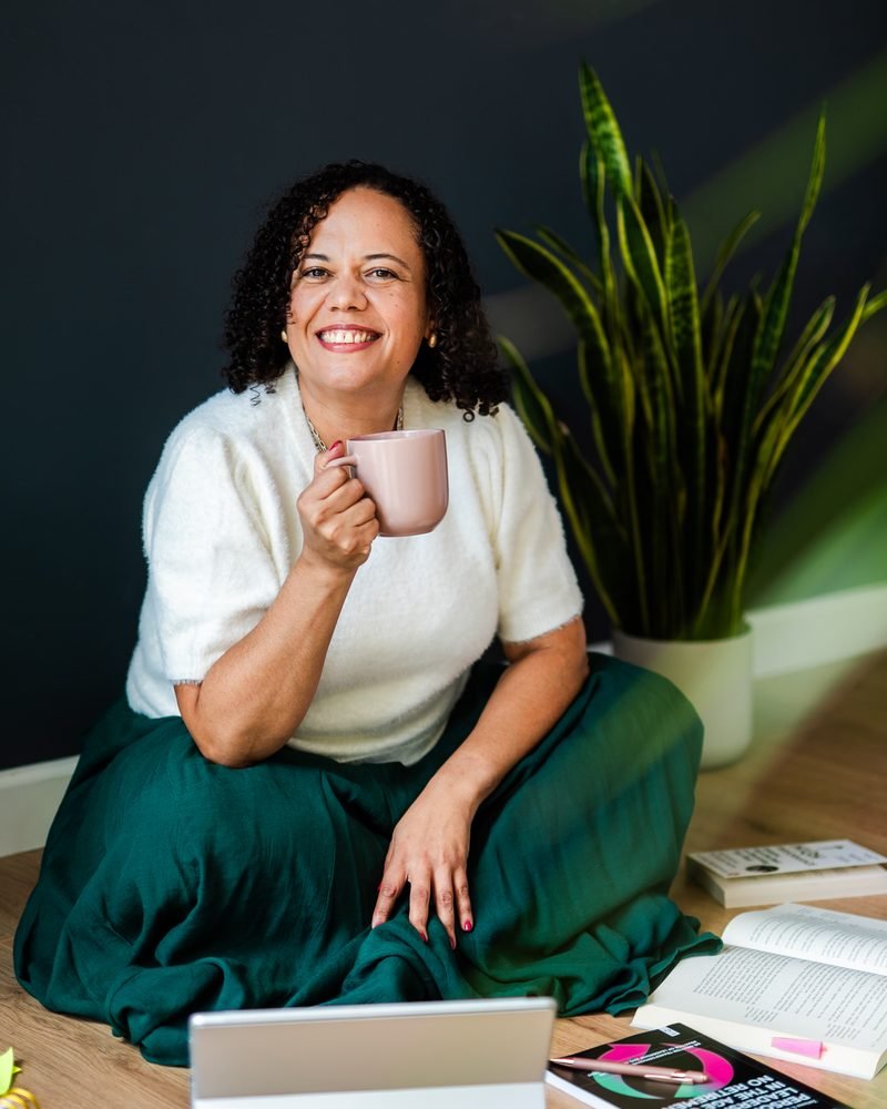 Alicia Noble sitting on the floor, smiling and holding a mug