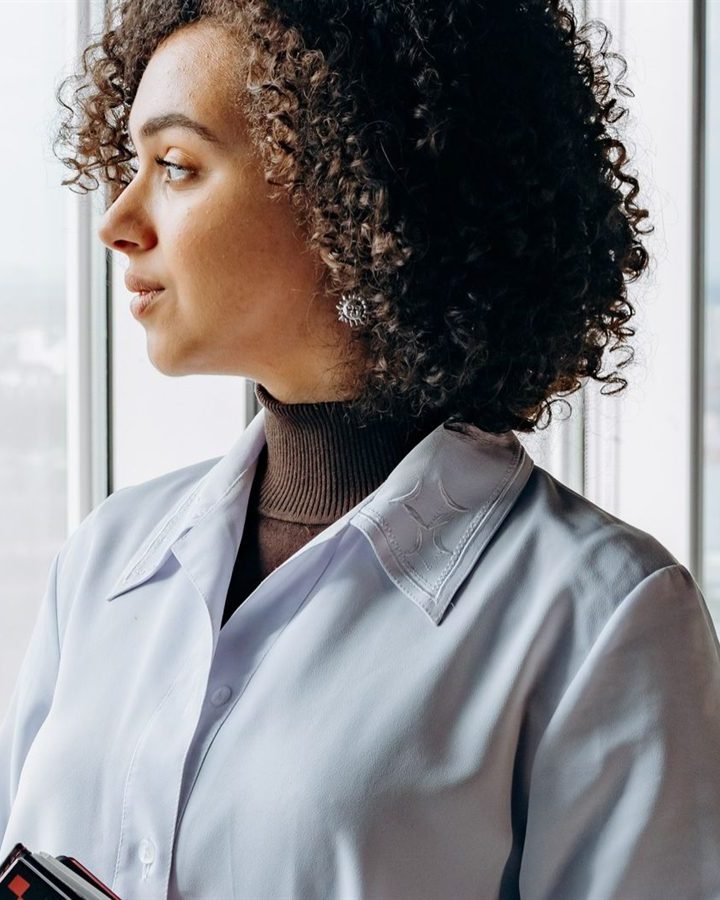 A woman with curly hair looking out of an office window, deep in thought