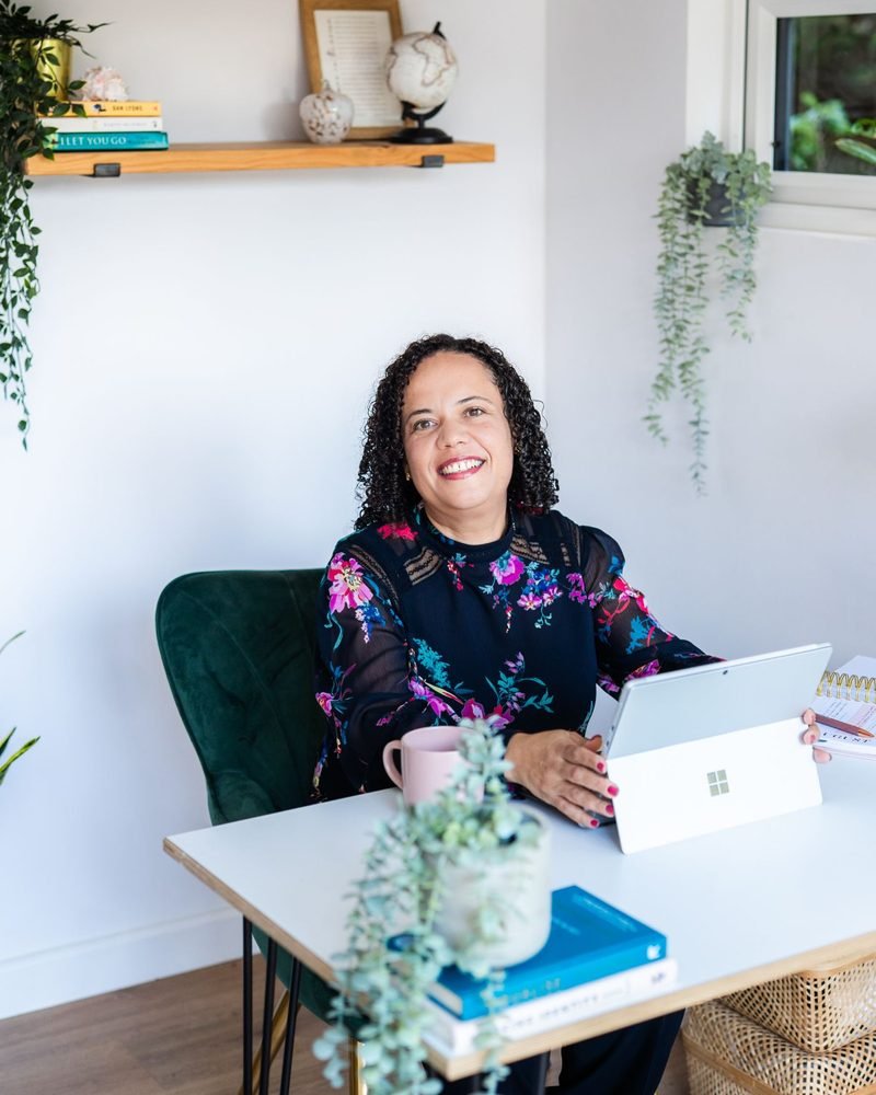 Alicia Noble smiling, sitting at a desk with a tablet and notebook
