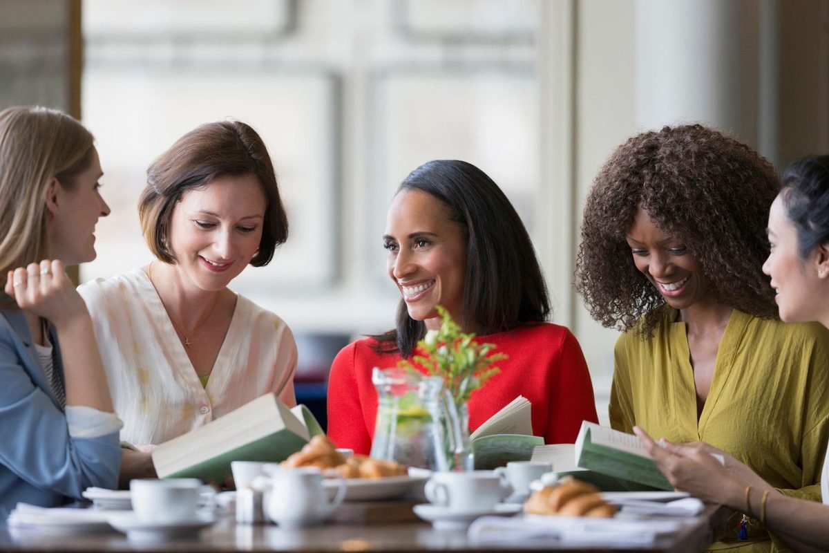 A small group of women talking around a table with books and coffee