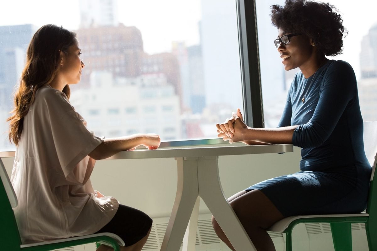 Two women in conversation at a table by a window